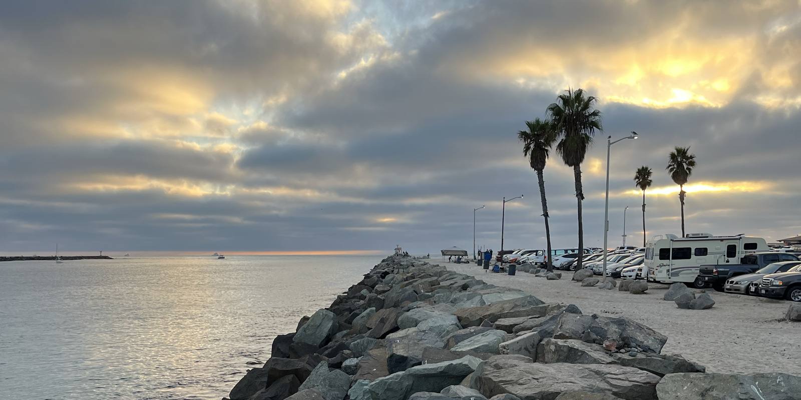 The rock jetty at Mission Beach with palm trees under a cloudy sunset sky